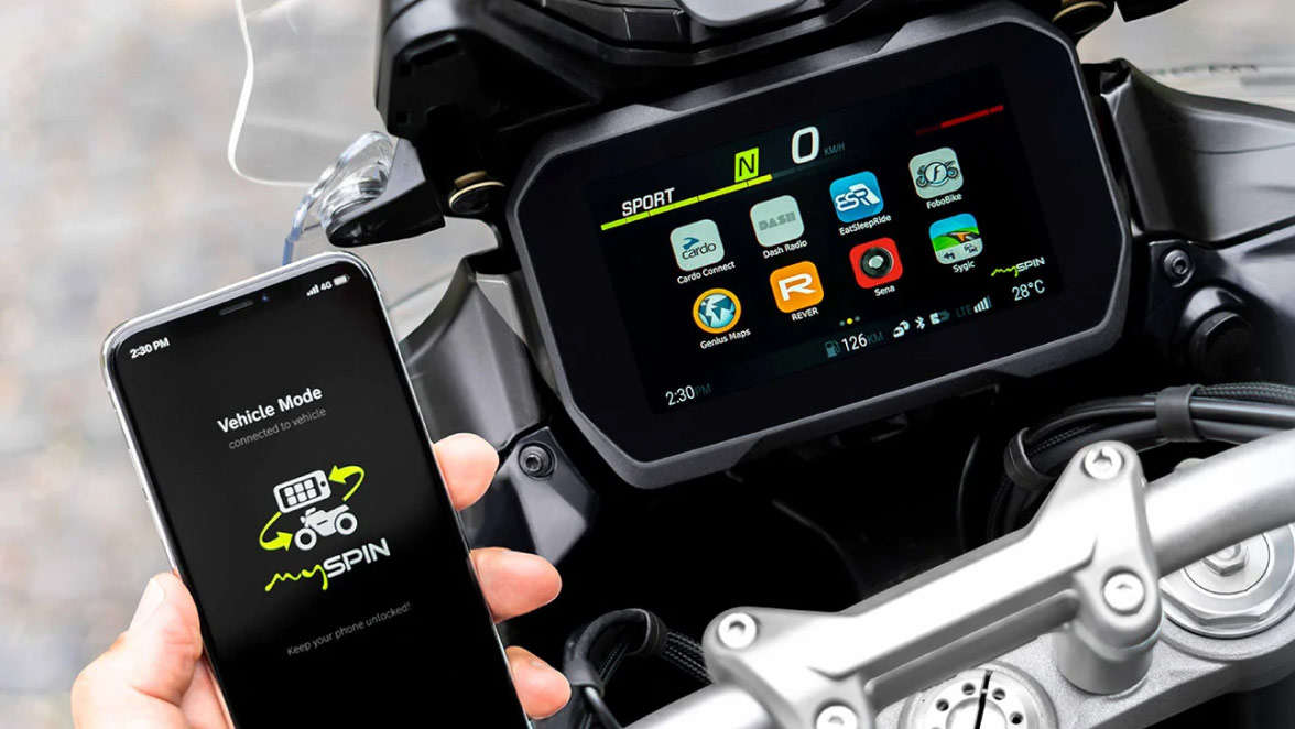 Close-up of a hand holding a smartphone next to motorcycle display